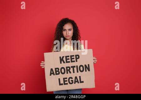 Eine afroamerikanische Frau mit Plakat und Phrase hält die Abtreibungsgesetze auf rotem Hintergrund. Schwangerschaftsabbruch-Protest Stockfoto