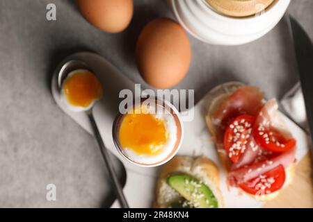 Frisch gekochtes Ei im Becher und Sandwiches auf grauem Tisch, flach liegend Stockfoto