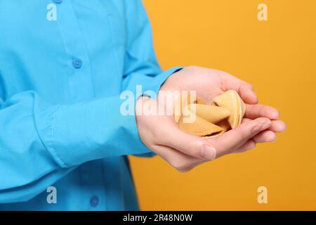 Junge Frau mit leckeren Glückskeksen, mit Prognosen auf gelbem Hintergrund, Nahaufnahme Stockfoto