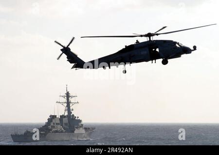 US Navy SH-60F Seahawk patrouilliert in den Gewässern hinter dem gesteuerten Raketenzerstörer USS Arleigh Burke (DDG 51) Stockfoto