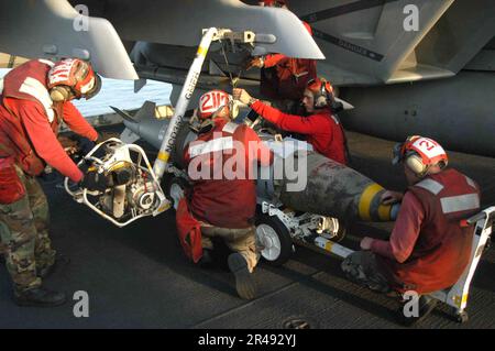 US Navy Aviation Ordnancemen, die dem Eagles of Strike Fighter Squadron One One Five (VFA-115) zugeteilt sind, bereiten sich darauf vor, eine Joint Direct Attack Munitions auf einem Flügelpylon einer F-A-18E Super Hornet während des Fluges zu heben Stockfoto