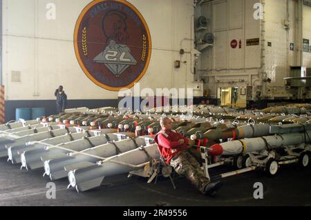 US Navy ein Mitarbeiter der Luftfahrtbehörde, der der Waffenabteilung an Bord der USS Abraham Lincoln (CVN 72) zugeteilt ist, beobachtet die in der Hangarbucht des Schiffs bereitgestellte Munition Stockfoto
