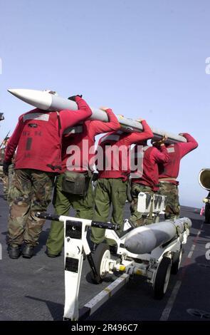 US Navy Aviation Ordnancemen heben eine fortgeschrittene, mittlere Luft-Luft-Rakete (AMRAAM) an, um sie an einem F-A-18 Hornet an Bord der USS Nimitz (CVN 68) zu befestigen. Stockfoto