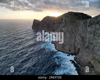 Ein Luftblick auf Meereswellen, die eine felsige Küste bei einem bewölkten Sonnenuntergang durchwühlen Stockfoto