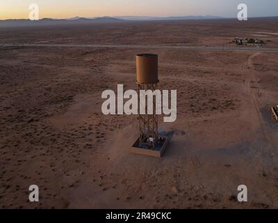 Ein rostiger Wassertank in einer trockenen Wüstenumgebung, umgeben von unfruchtbarem Gelände Stockfoto