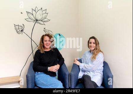 Während einer Arbeitspause lächelnde weibliche Mitarbeiter, die sich entspannen und auf Sesseln sitzen. Stockfoto