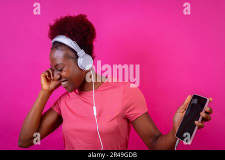 Ein Porträt einer jungen, fröhlichen schwarzen Frau, die Musik mit Kopfhörern hört Stockfoto