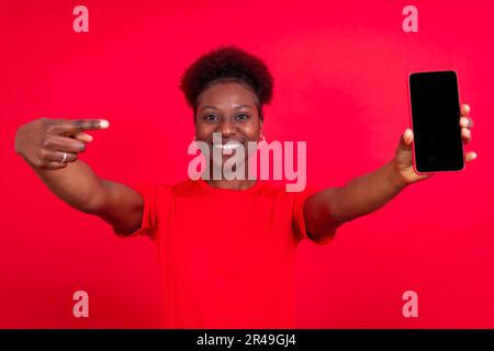 Eine junge Frau, die ein Smartphone in der Hand hält, ein Selfie macht und in die Kamera lächelt Stockfoto