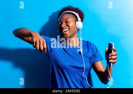 Ein Porträt einer jungen, fröhlichen schwarzen Frau, die Musik mit Kopfhörern hört Stockfoto