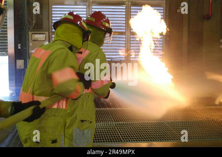 MATROSEN der US-Marine, die dem Amphibiendock-Landungsschiff USS Fort McHenry (LSD 43) zugeteilt sind, handhaben während der Feuerbekämpfungsschulung in der Yokosuka afloat Training Group einen voll aufgeladenen Feuerwehrschlauch bei einem Brand der Klasse Alpha Stockfoto