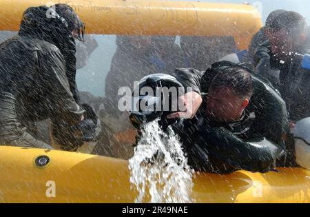 US Navy ein Überlebenschüler der Luftfahrt holt Wasser aus dem Rettungsfloß während eines Sturmszenarios, das als Teil eines Auffrischungslehrgangs stattfindet Stockfoto