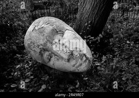 Eine Nahaufnahme einer in Graustufen geschnitzten Maskenskulptur auf einem Parkboden Stockfoto