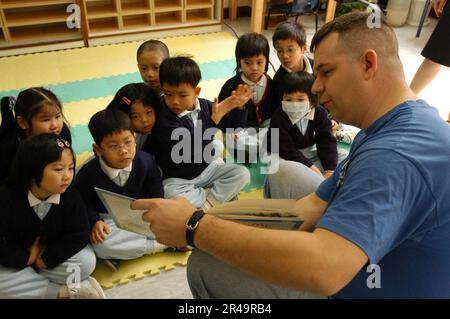 US Navy Master Chief Information Systems Technician liest Kindern in einer Kindertagesstätte in Hongkong vor. Stockfoto