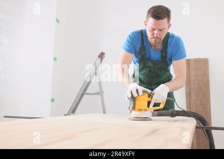 Zimmermann poliert Holzschreibtisch mit moderner Schleifmaschine Stockfoto
