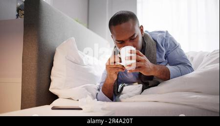 Kranker Mann, Der Auf Dem Bett Sitzt Und Eine Tasse Tee Hält Stockfoto