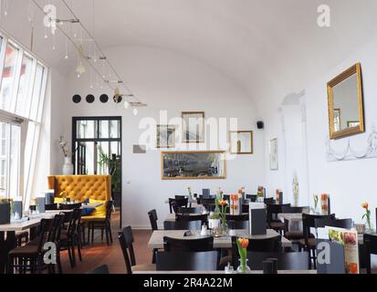 Ein Innenraum mit mehreren Tischen und Stühlen in einem großen Raum mit vielen Fenstern und heller Beleuchtung Stockfoto