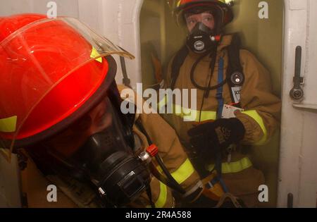 US Navy Machinery Reparateur 1. Klasse A Leiter des Feuerteams verlässt einen Raum nach der Untersuchung auf Feuer und Schäden, während Machinist Mate 3. Klasse während einer General Qua auf Reflash achtet Stockfoto
