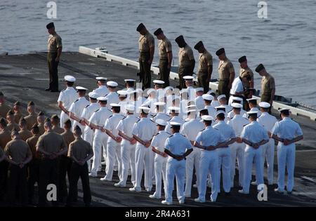 US Navy Matrosen und Marines verneigen sich vor Respekt während einer Kranzlegzeremonie, die zu Ehren auf dem Flugdeck stattfindet Stockfoto