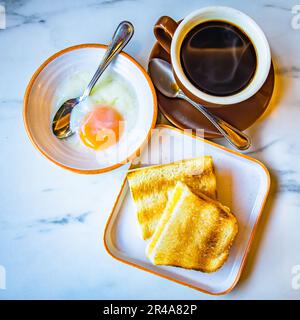 Traditionelles Café, Frühstück. Schwarzer Kaffee, halb gekochte Eier und Toast. Authentisches hainanisches Essen. Stockfoto