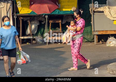 SAMUT PRAKAN, THAILAND, 03 2023. MÄRZ, eine Frau trägt ein Baby auf einer Straße mit einem Marktplatz Stockfoto