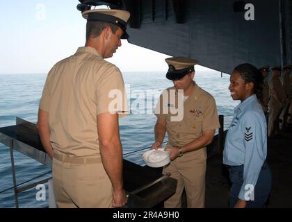 US Navy Information Systems Technician 1. Klasse rechts, sieht als Kommandomeisterzentrum und legt ihren weißen Hut auf die zeremonielle Folie Stockfoto