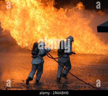 US Navy zwei Aviation Boatswain's Mate Studenten machen einen Angriff auf ein großflächiges Scheinflugzeug Feuer an Bord des Goodfellow Air Force Base, Texas Stockfoto