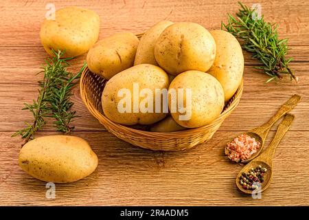 Eine Nahaufnahme von Kartoffeln in einem Korb mit zwei Löffeln Gewürzen und Rosmarin daneben Stockfoto