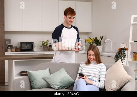 Ein junger Mann, der seiner Freundin einen Antrag macht, mit einem Handy in der Küche Stockfoto