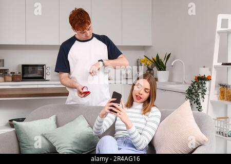 Wartender junger Mann, der seiner Freundin einen Heiratsantrag macht, mit Handy in der Küche Stockfoto
