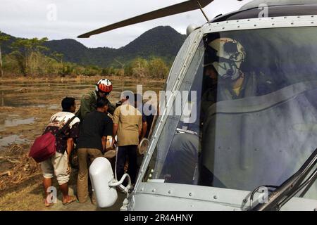 MATE 1. Klasse des US Navy Aviation Machinisten links, spricht mit indonesischen Einheimischen, während er Essen verteilt, während LT. Über seine Schulter wacht Stockfoto