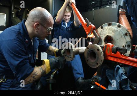 US Navy Hull Maintenance Technician 1. Class Left, heizt eine Mutter an einer Dampfspule mit einem Lötbrenner auf, während Hull Maintenance Technician 3. Class Stockfoto