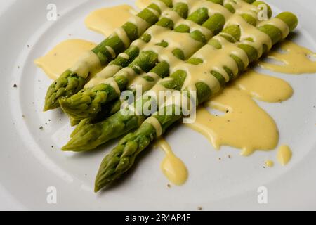 Grüner Spargel mit Sauce Hollandaise, serviert auf einem weißen Teller Stockfoto