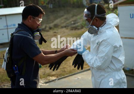 US Navy Chief Hospital Corpsman verließ, hilft Hospital Corpsman 2. Klasse, während er seine persönliche Schutzausrüstung für das Sprühen von Pestiziden donnert. Stockfoto