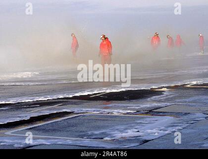 US Navy-Matrosen, die an Bord der USS Dwight D. Eisenhower (CVN 69) den Air and Engineering Departments zugeteilt sind, testen die Gegenmaßnahme „Wash-Down“-Sprinkleranlage auf dem Cockpit während eines Flugzeugs der Nimitz-Klasse. Stockfoto