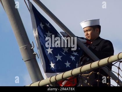 LAGERHAUS der US Navy 3. Klasse, das dem Amphibiendock-Landungsschiff USS Fort McHenry (LSD 43) zugewiesen ist, bereitet sich darauf vor, die amerikanische Flagge in den Morgenfarben zu hissen. Stockfoto