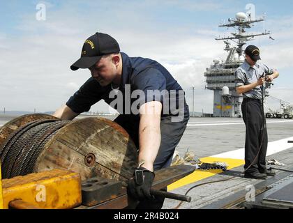 US Navy Two Aviation Boatswain arbeitet zusammen, um ein Rückzugskabel in einen von vier dampfbetriebenen Katapulten an Bord des Flugzeugträgers USS Abraham Lincoln (CVN 72) der Nimitz-Klasse zu verlegen. Stockfoto