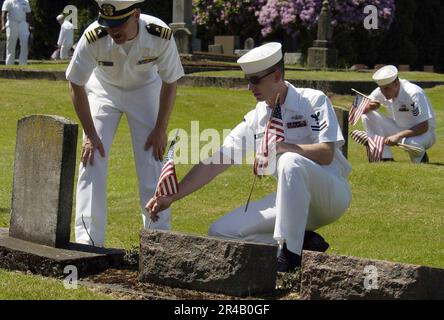 MARINESTÜTZPUNKT Everett Chaplain, Lieutenant Commander. Und Ingenieurassistent der 2. Klasse setzt eine amerikanische Flagge auf den Grabstein eines Veteranen. Stockfoto