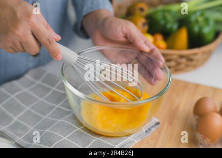 Junge Frau, die in einer hellen Küche kocht, Hände, die Eier in einer Schüssel auf ein Handtuch und einen Holztisch legen. Zutaten für gesundes Kochen zubereiten. Nach Hause Stockfoto