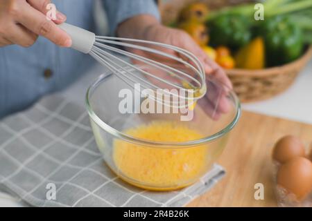 Junge Frau, die in einer hellen Küche kocht, Hände, die Eier in einer Schüssel auf ein Handtuch und einen Holztisch legen. Zutaten für gesundes Kochen zubereiten. Nach Hause Stockfoto