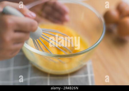 Junge Frau, die in einer hellen Küche kocht, Hände, die Eier in einer Schüssel auf ein Handtuch und einen Holztisch legen. Zutaten für gesundes Kochen zubereiten. Nach Hause Stockfoto