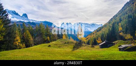 Diese Luftaufnahme erfasst ein atemberaubendes Tal mit üppigem grünen Gras und Holzbänken, umgeben von majestätischen Bergen im Hintergrund Stockfoto