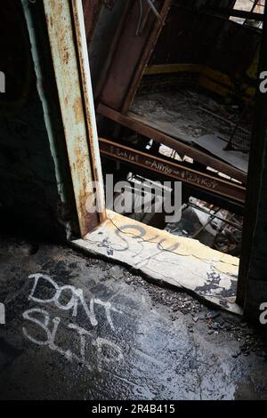 Eine Nahaufnahme eines Graffiti-Wandbildes auf dem Boden eines verlassenen Gebäudes mit einem sichtbaren Eingang Stockfoto