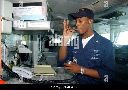 US Navy Boatswain's Mate 3. Class pfeift über die 1MC und signalisiert den Beginn der morgendlichen Ankündigungen, während Boatswain Mate von der Uhr steht. Stockfoto