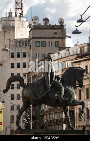 Eine Nahaufnahme einer majestätischen Bronzestatue, die einen Mann darstellt, der vor einem Hintergrund moderner Gebäude auf einem Pferd reitet Stockfoto