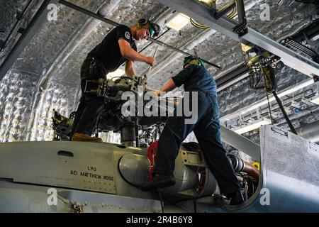 SINGAPUR (7. März 2023) Aviation Machinist’s Mate 3. Class Brendon Johnson, Left, from Queen Creek, Arizona, und Aviation Machinist’s Mate 1. Class Alexander Rauchfuss, from Denver, beide der Helicopter Maritime Strike Squadron (HSM) 35 zugewiesen, deinstallieren eine Hauptrotorschaufel von einem MH-60R SeaHawk, das an HSM 35 angeschlossen ist, Während der Wartung in der Hangarbucht an Bord des Küstenschiffes USS Oakland (LCS 24) der Unabhängigkeitsklasse in Singapur, 7. März 2023. Oakland, Teil der Destroyer-Geschwader 7, ist im Rotationseinsatz und operiert im US-7.-Flottengebiet, um die Interoper zu verbessern Stockfoto