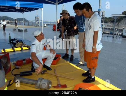 US Navy Damage Controlman 3. Class erklärt einer Gruppe japanischer Besucher die Ausrüstung zur Schadensbegrenzung, während sie das Hauptdeck besichtigen. Stockfoto