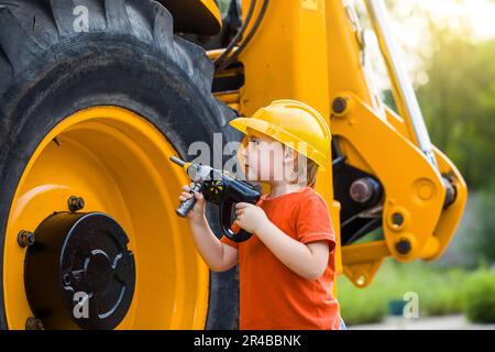 Kleiner Junge mit Spielzeugwerkzeugen in der Garage. Der Sohn hilft dem Vater bei der Reparatur des Traktors. Beziehen Sie das Kind in die Arbeit ein Stockfoto