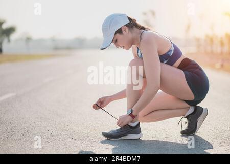 Eine junge asiatische Frau bindet ihre Schuhschnürsenkel, während sie sich auf einen Lauf vorbereitet Stockfoto