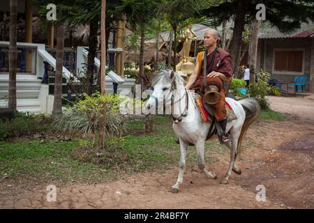 CHIANG RAI, THAILAND - 21. Mai 2016: Junger buddhistischer Mönch auf einem Pferd im Tempel des Goldenen Pferdes (Wat Phra Archa Thong). Mönch in traditionellem rotem Bademantel A. Stockfoto