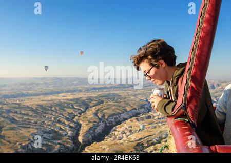 Junge Frau im Heißluftballonkorb, die sich Luftballons und die wunderschöne Landschaft von Goreme ansieht, Reiseurlaub in Kappadokien, Türkei Stockfoto